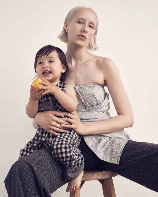 Woman and child sit together in a studio setting. The child is holding an apple. Both are wearing neutral tone clothing.