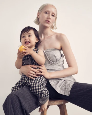 Woman and child sit together in a studio setting. The child is holding an apple. Both are wearing neutral tone clothing.