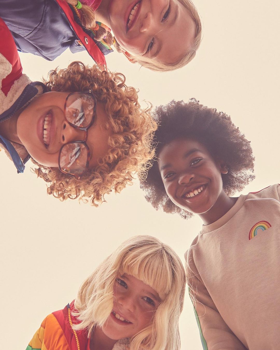 Four smiling children huddle closely together, looking down at the camera with bright expressions in an eye-level, close-up composition.