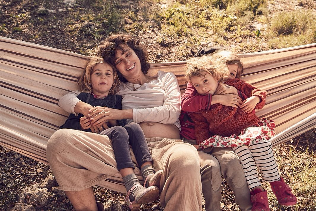 A mother with her three young children sitting in a hammock outdoors. The children are cuddling with their mother in a daytime shot.