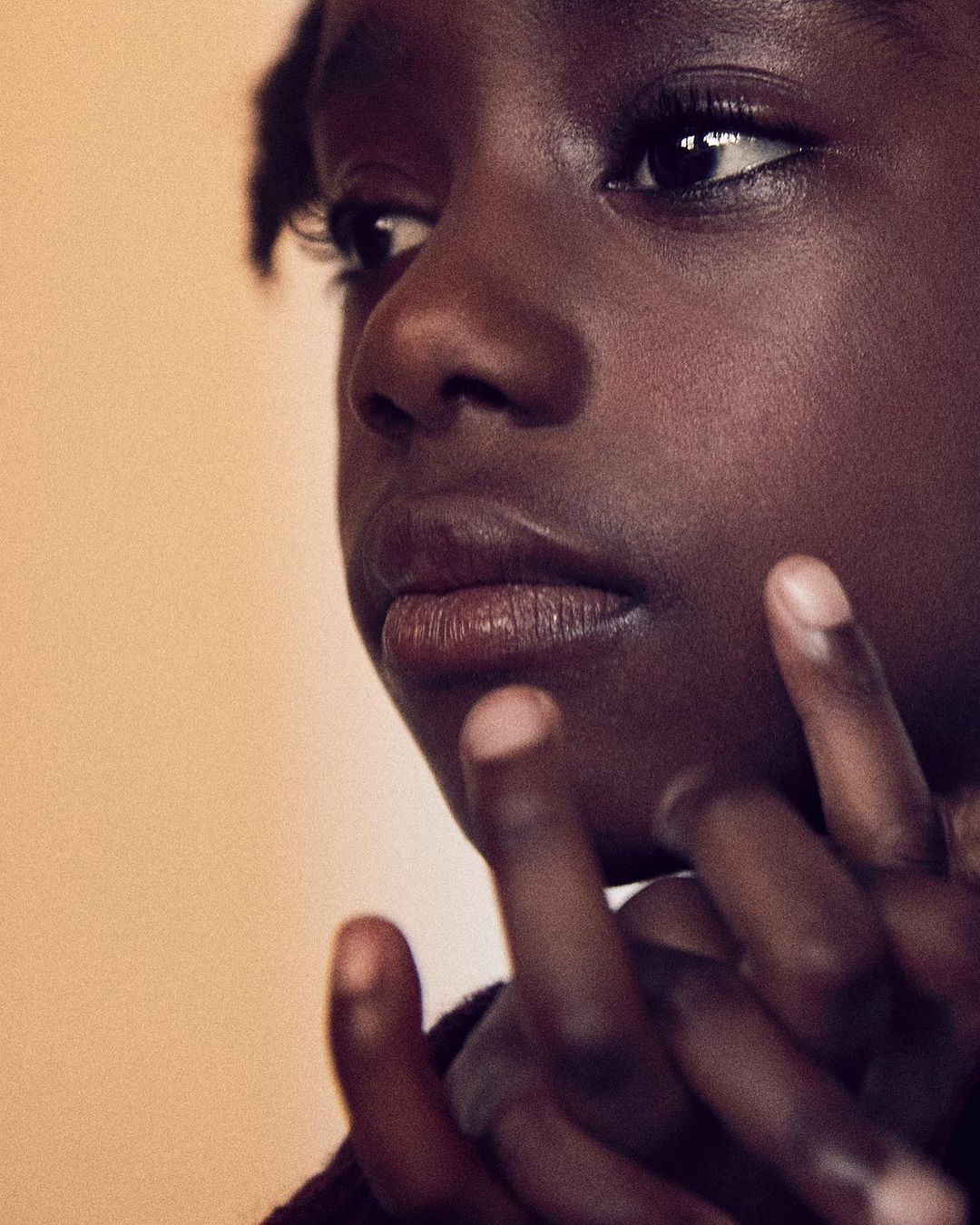 Close-up studio portrait of a young African American girl with dark skin, looking to the side with fingers near her face.