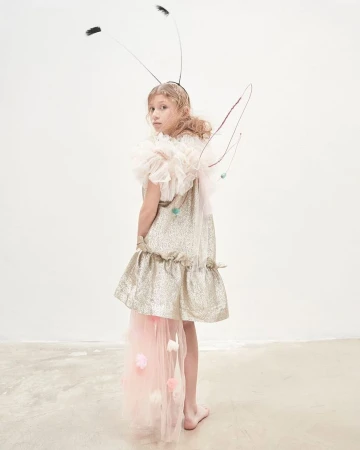 Young model wearing a sparkly dress and bug antennae headband with wire wings against a white seamless background