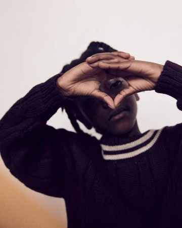 Portrait of a person wearing a dark sweater with hands framing their face in London