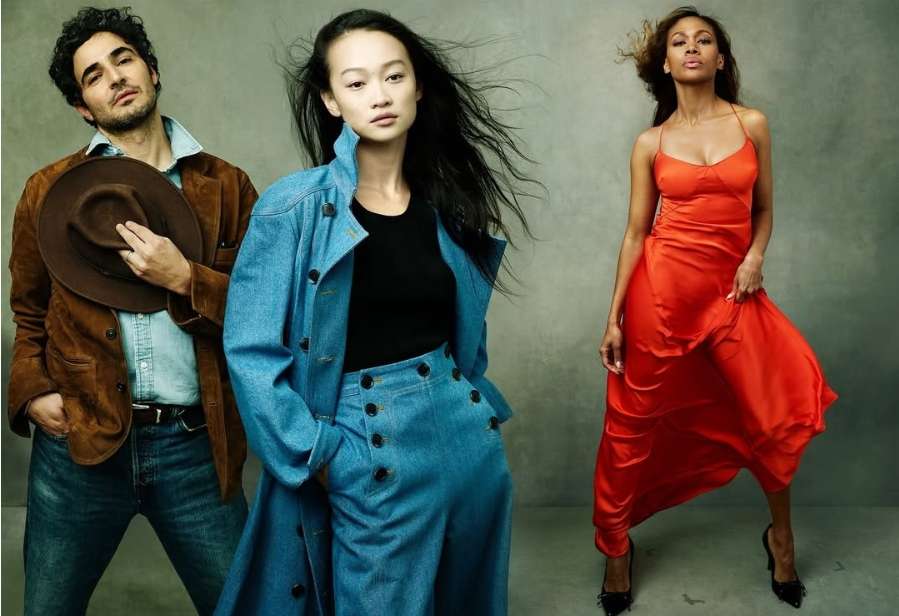 Three diverse fashion models strike a pose in a studio, wearing stylish outfits in an eye-level shot against a neutral gray backdrop.