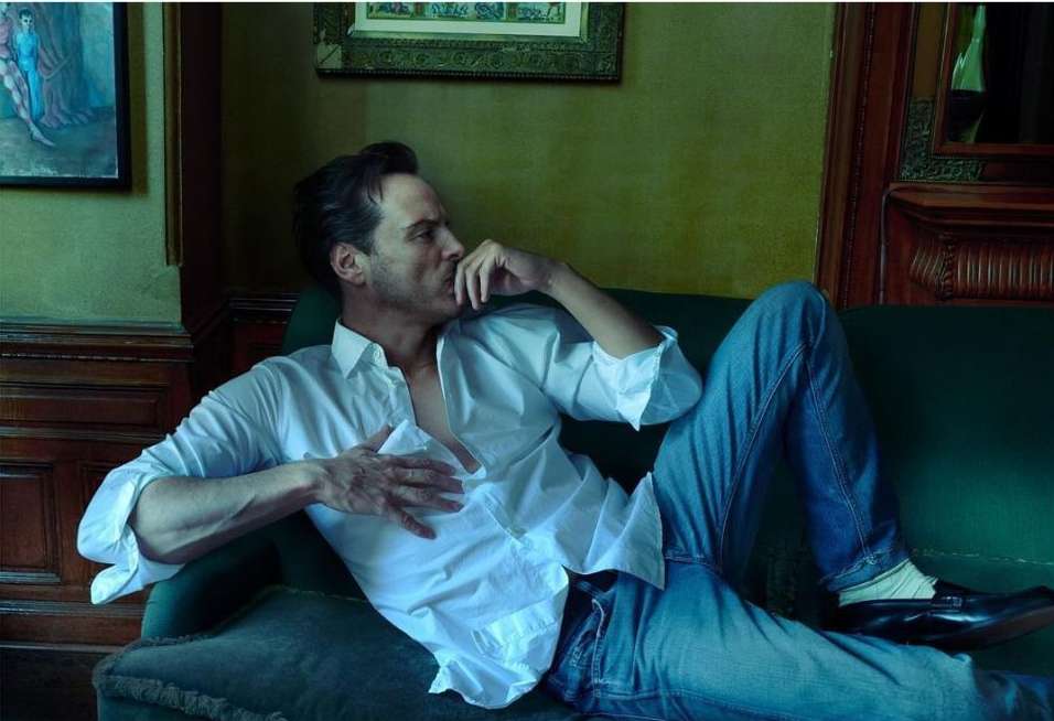 Man in a white shirt and blue jeans reclining on a green sofa in an interior setting