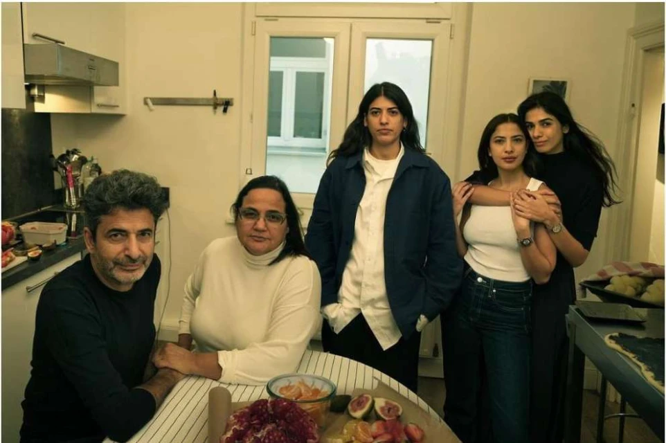Group of five people in a kitchen setting with a table of food, including three adult women, one adult male, and one adult female.