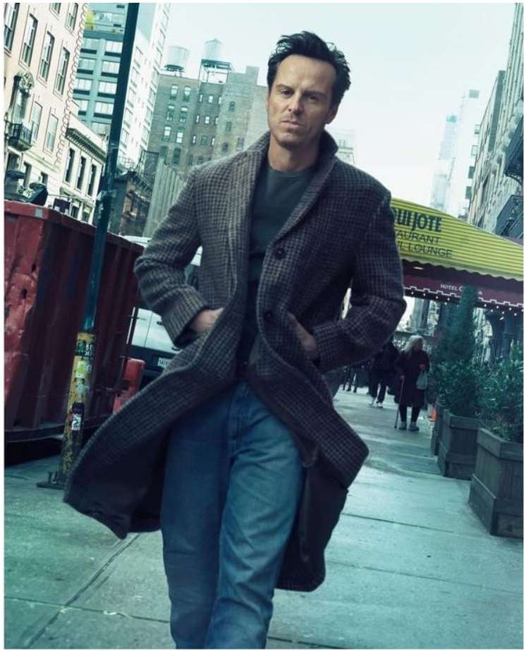 Man in tweed coat walks on a city street, hands in pockets, buildings and street in the background, medium shot, lifestyle.