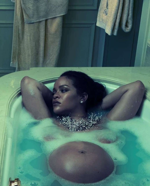 Pregnant woman, lying back in a bathtub filled with bubble bath, wearing a beaded necklace and earrings in a turquoise-toned bathroom.