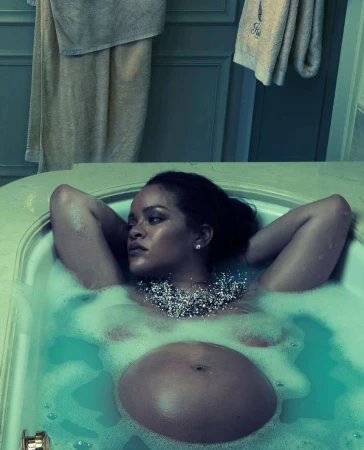 Pregnant woman, lying back in a bathtub filled with bubble bath, wearing a beaded necklace and earrings in a turquoise-toned bathroom.