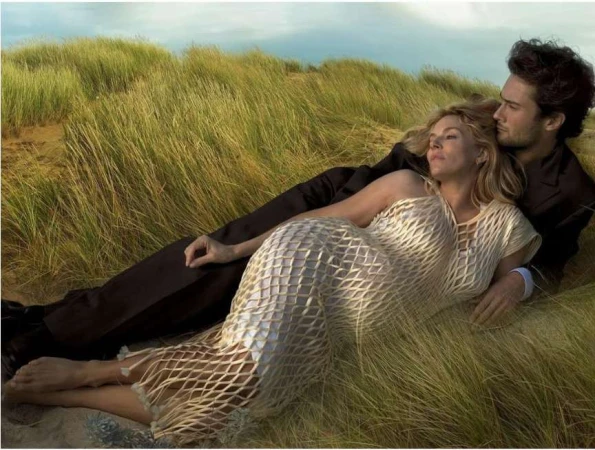 A man and a woman lying closely together among tall beach grass against an overcast sky, captured by Annie Leibovitz.