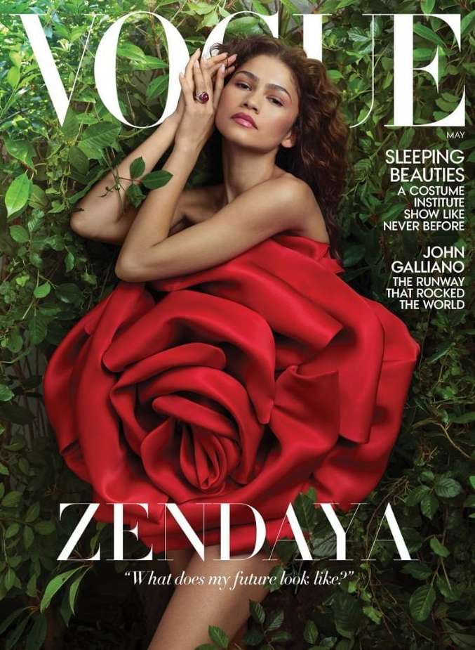 Zendaya on Vogue cover, wearing a red flower-shaped dress, lying amongst green leaves. Magazine cover with large white text.
