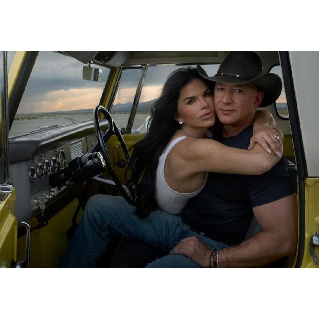 Couple embraces in a yellow off-road vehicle in a desert landscape with stormy skies. Man in cowboy hat and woman wearing a white top.