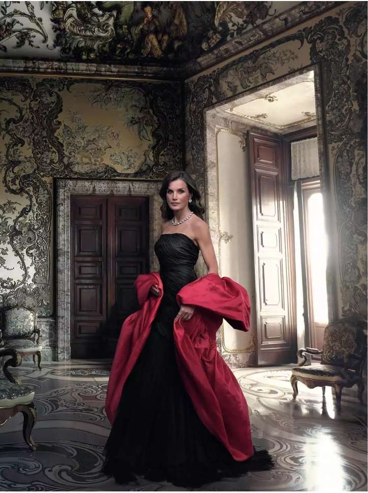 Elegant woman in a black strapless gown with a red shawl in a detailed, ornate room with high ceilings and classic architecture.
