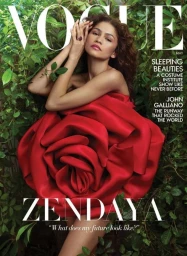 Zendaya posing amidst lush green foliage wrapped in a large sculptural red silk rose dress for a magazine cover portrait.