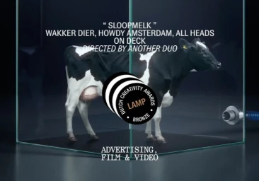 A black and white dairy cow standing inside a transparent glass display enclosure on a dark studio floor.