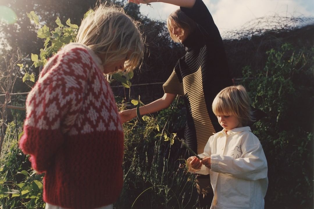 Three people in a garden setting. One person wearing a red and white patterned sweater, another in a black and olive top, and a child.