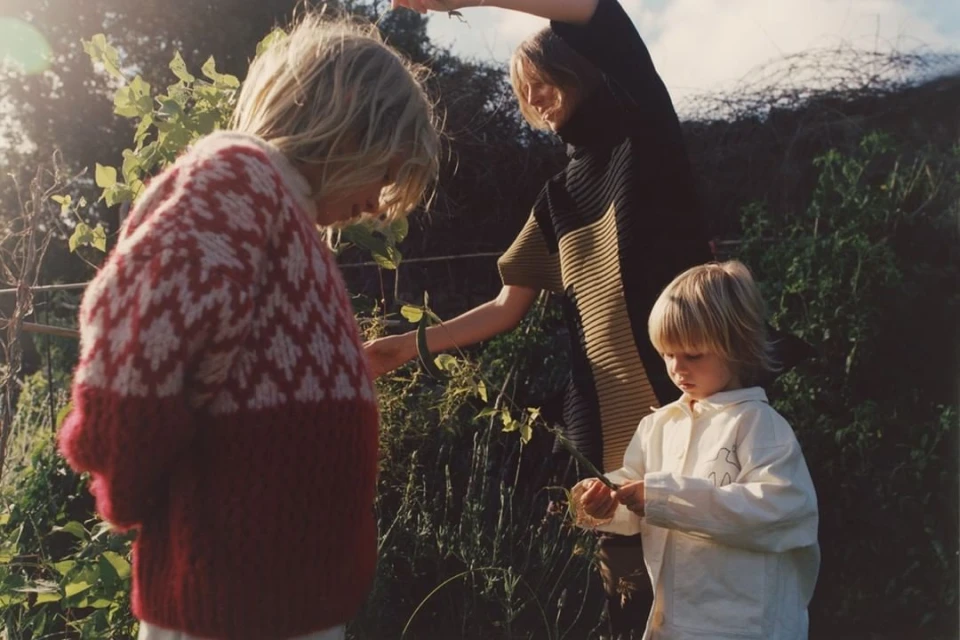 Three people in a garden setting. One person wearing a red and white patterned sweater, another in a black and olive top, and a child.