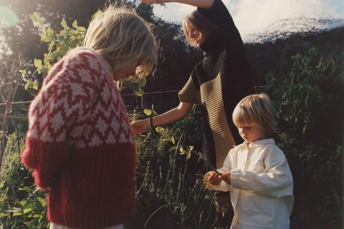 Three people in a garden setting. One person wearing a red and white patterned sweater, another in a black and olive top, and a child.