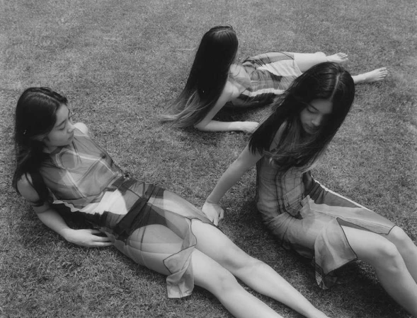 Three young women in sheer dresses lying on a grass lawn in a black and white photograph by Anouk Nitsche.