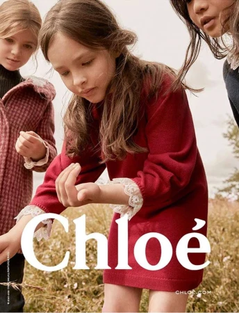 Three young girls outdoors in an outdoor field wearing red and patterned dresses, photographed by Anouk Nitsche.