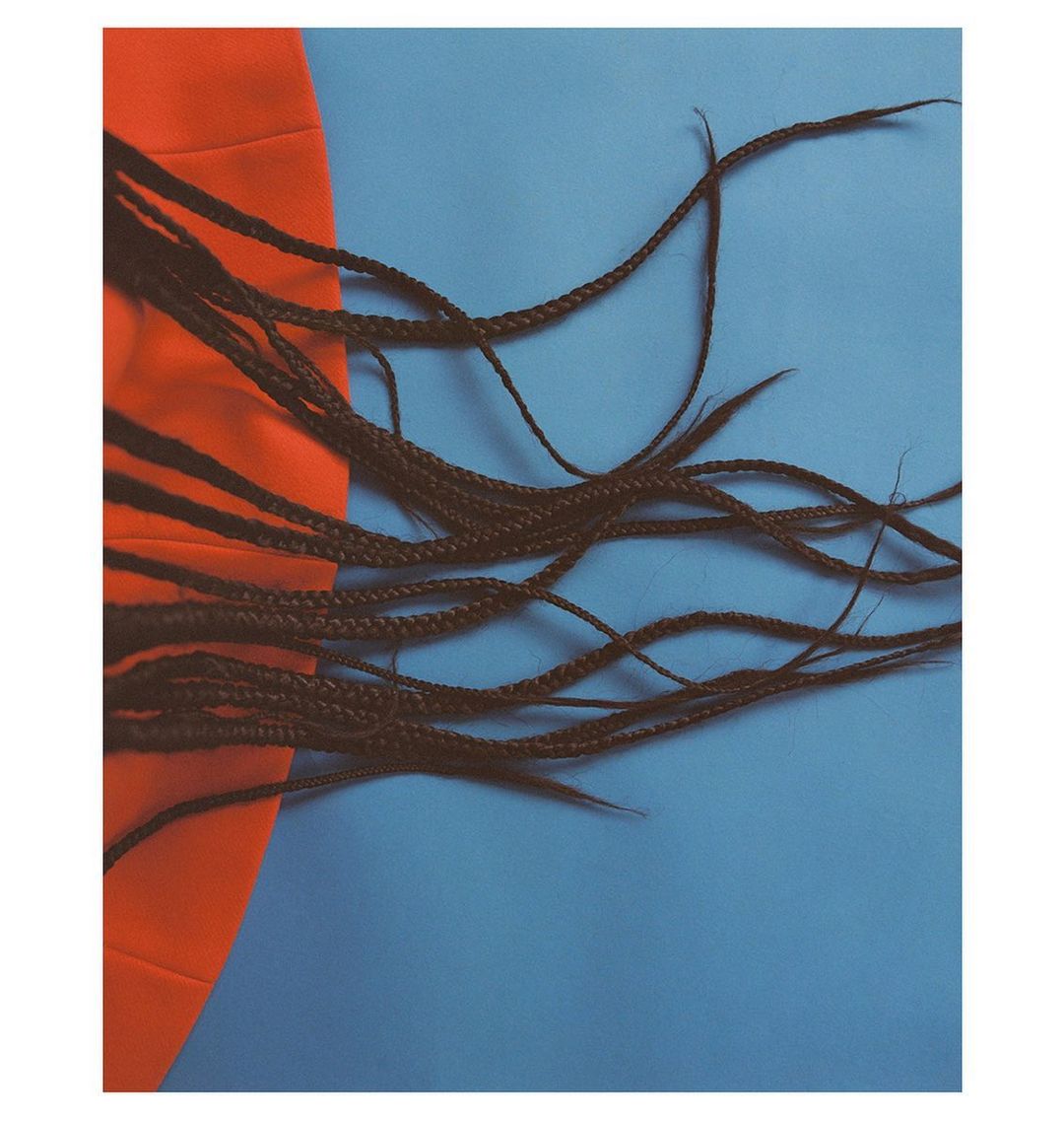 Artful shot of long braided hair partially draped across an orange cloth against a light blue backdrop, fashion-forward.