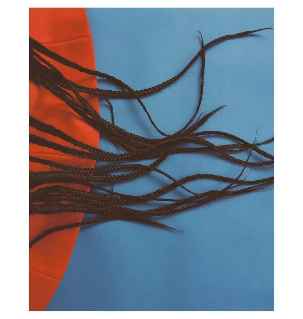 Artful shot of long braided hair partially draped across an orange cloth against a light blue backdrop, fashion-forward.