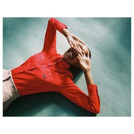 Model wearing a vibrant red long-sleeve shirt lying on a teal textured surface in Paris by Anouk Nitsche