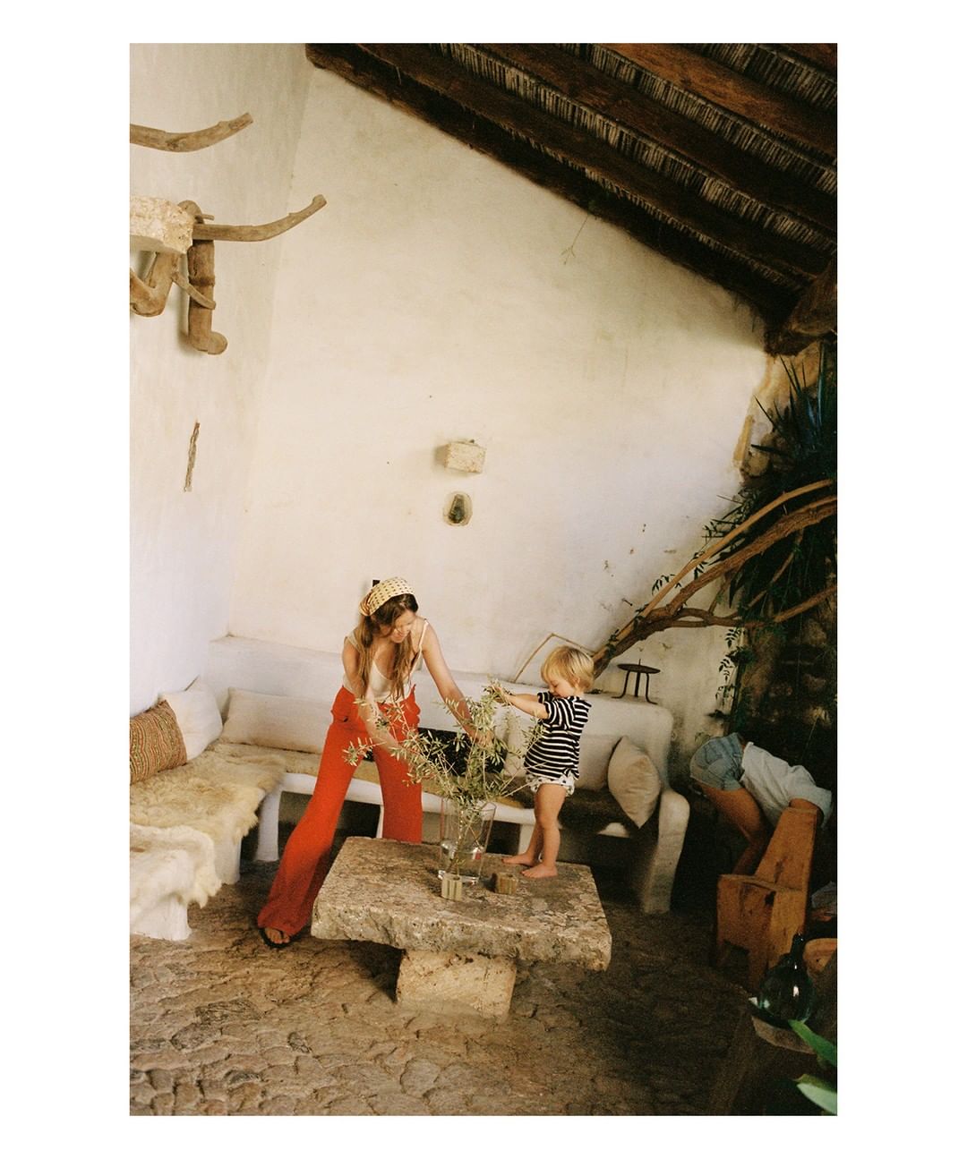 Indoor family scene featuring an adult female and a toddler arranging flowers on a stone table, with natural light and rustic interior.