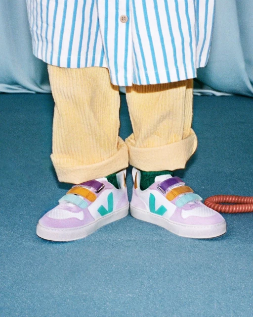 A person is wearing white sneakers with a colored stripe design, yellow corduroy pants, and a striped shirt, showcasing a trendy style.