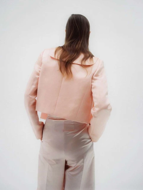 Back view of a woman in a peach blazer and pants standing against a white background, fashion photography, studio shot.