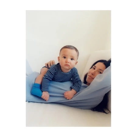 Baby in striped shirt lying on woman wearing blue top on white sofa, photographed in Paris by Anouk Nitsche.