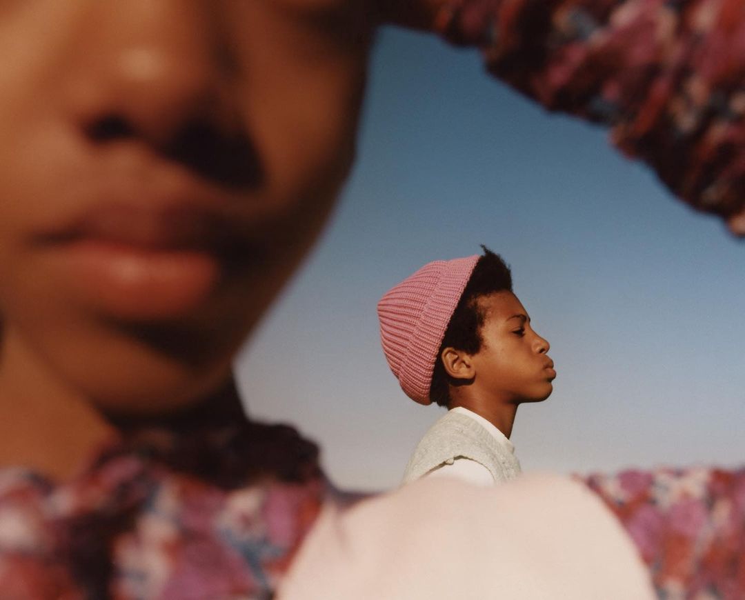 Two young African-descent children in a portrait. One wears a pink knit hat against a clear blue sky on a sunny day.