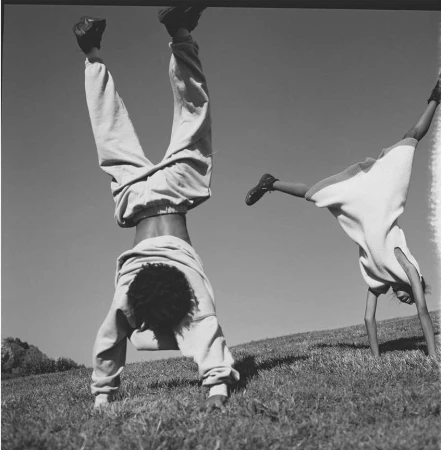 Two people doing handstands on a grassy hill under an open sky in a black and white photograph by Anouk Nitsche.