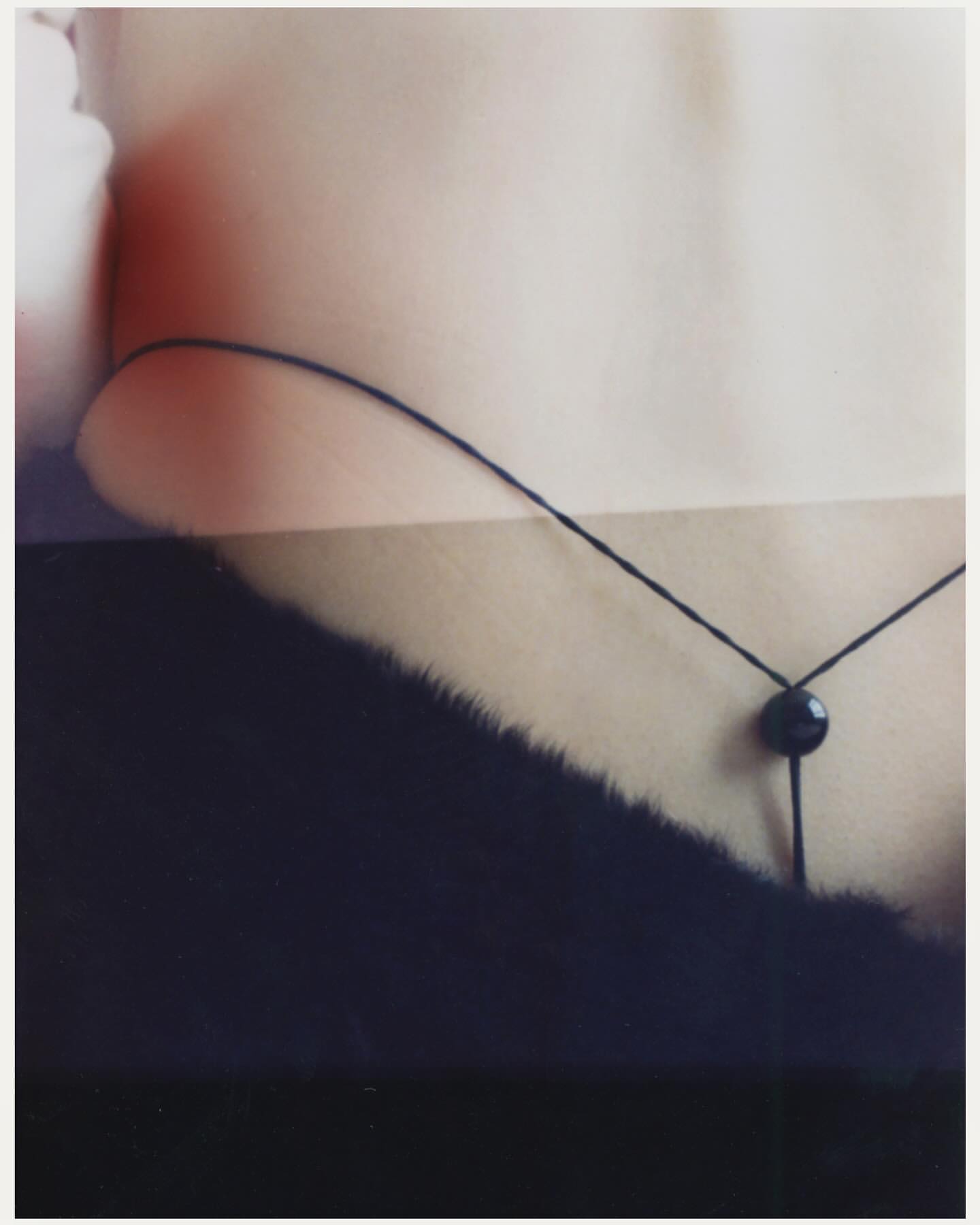 Close-up photograph of a person's back, a delicate black string, and dark fur with a light skin background.