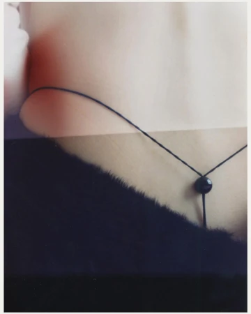 Close-up photograph of a person's back, a delicate black string, and dark fur with a light skin background.