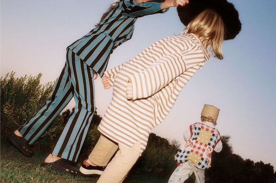Three kids in retro striped outfits stand on a grassy hill under a bright blue sky, showcasing a vintage fashion editorial.