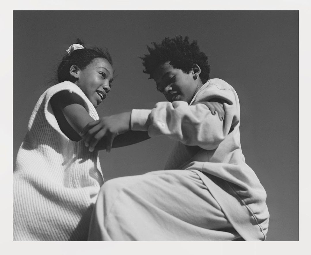 Black and white photograph of two children interacting closely, with a clear sky in the background. Youthful, playful connection captured.