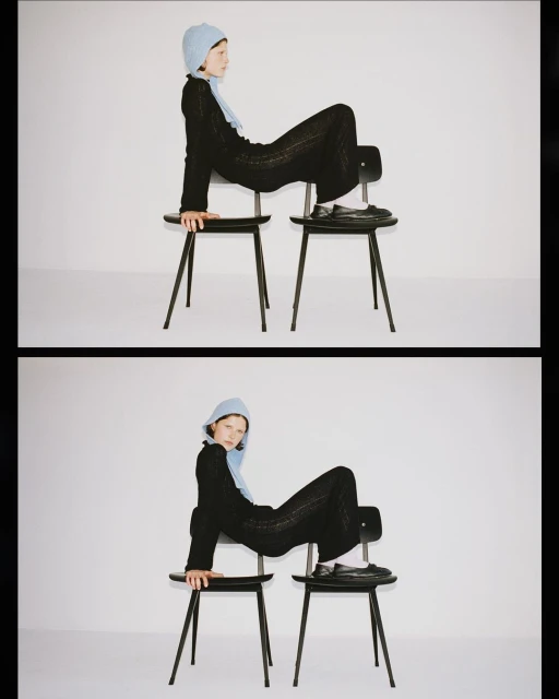Adult female in a black knit outfit and light blue bonnet sits on two black chairs in a bright studio with a minimalist aesthetic.