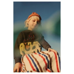 Child wearing an orange beanie and dark sweatshirt with a leopard print crossbody bag against a blue sky