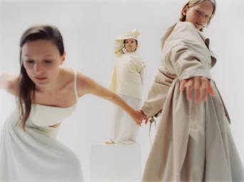 Three models in cream and beige attire posing against a plain white studio background in a fashion photograph by Anouk Nitsche