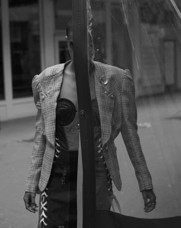 Model wearing a plaid blazer and lace-up denim top photographed behind a vertical reflective plastic barrier