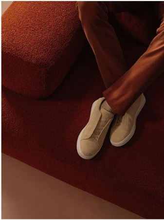 Close-up of cream sneakers and brown trousers on a textured rust-coloured upholstered sofa by Ansgar Sollmann