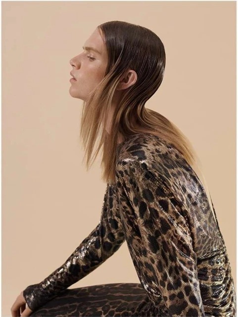 Side profile studio shot of a fair-skinned woman with wet-look brown and blonde hair wearing a long-sleeved leopard print dress.