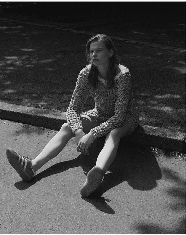 Young woman in a textured knit sweater seated on a curb outdoors, photographed in monochrome by Ansgar Sollmann in Frankfurt.