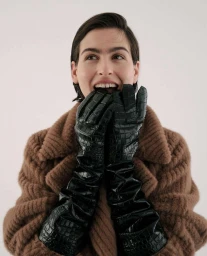 Smiling woman wearing long black leather gloves and a brown textured coat against a plain white background