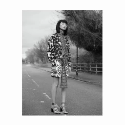 Monochrome fashion portrait of a woman standing on an asphalt road wearing a patterned jacket and heels by Ansgar Sollmann.