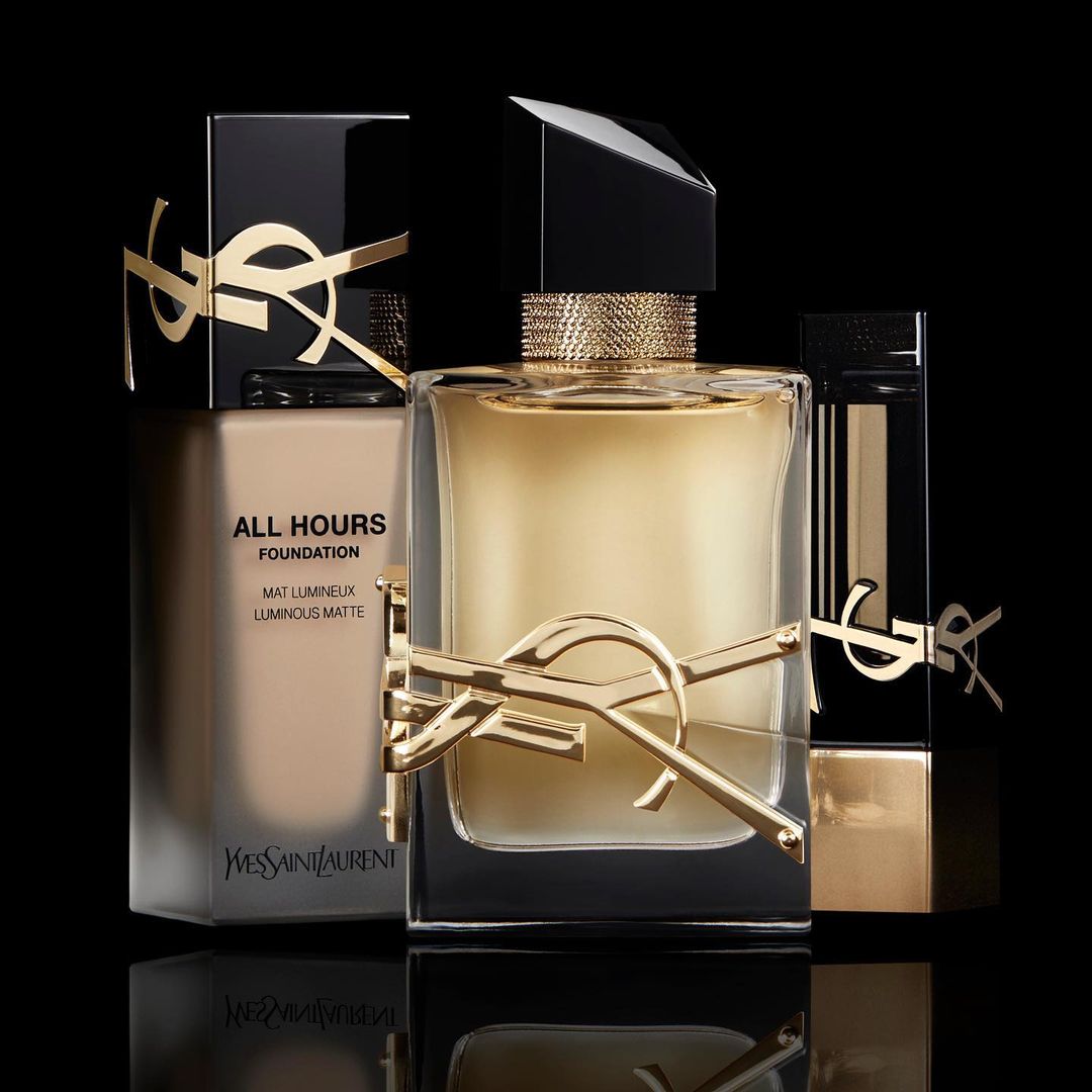 Still life shot of YSL beauty products including All Hours foundation, Libre eau de parfum, and Rouge Volupte Shine lipstick.