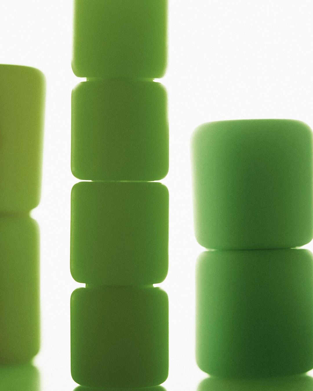 Close-up studio shot of stacked green cube shapes on a reflective surface, showcasing color and form against a white background.