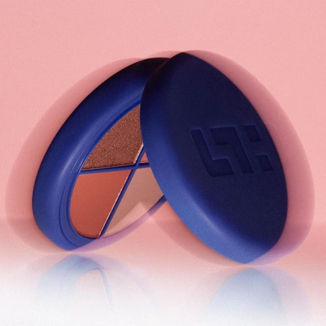 Close-up studio shot of a blue eyeshadow compact palette with warm-toned colors against a soft pink backdrop. Beauty product.