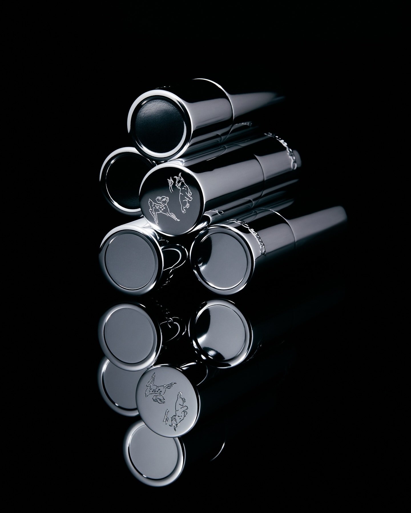 Stack of chrome metal lipstick cases or similar cosmetic containers on a black reflective surface, product photography, dark studio lighting.